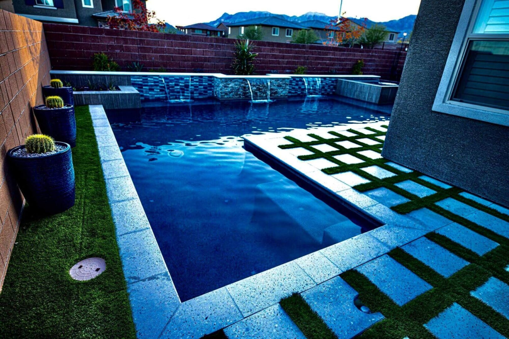 A pool with a tile border and grass on the ground.