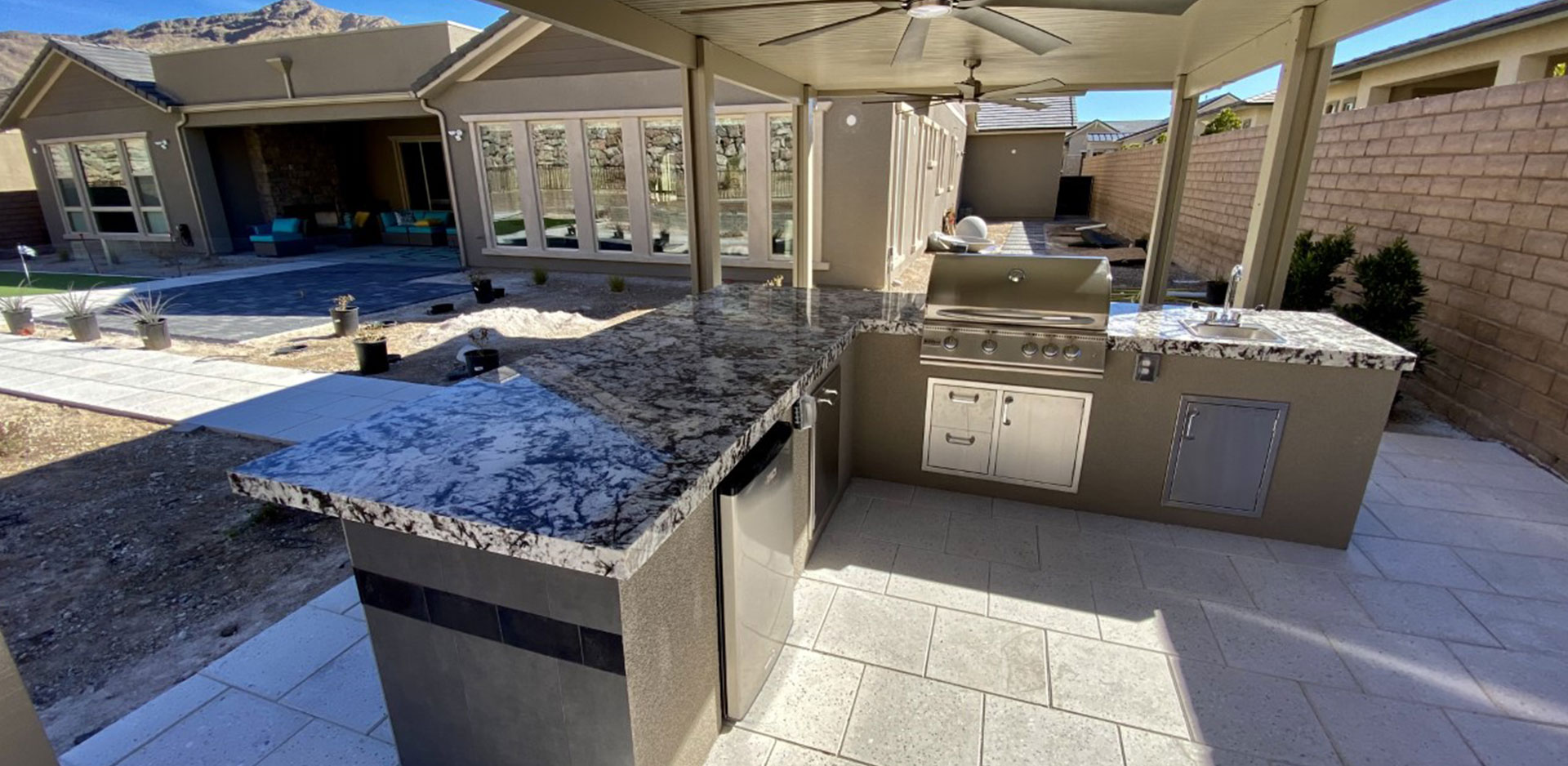 A large outdoor kitchen with an umbrella over the grill.