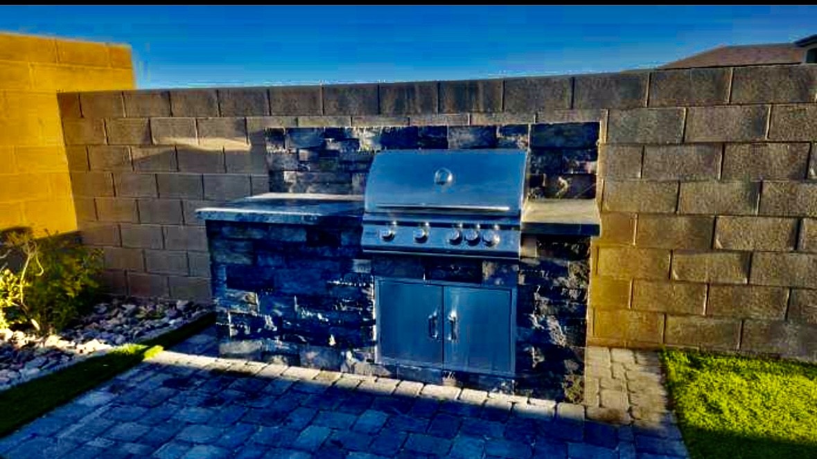 A grill and an outdoor kitchen with blue stone walls.