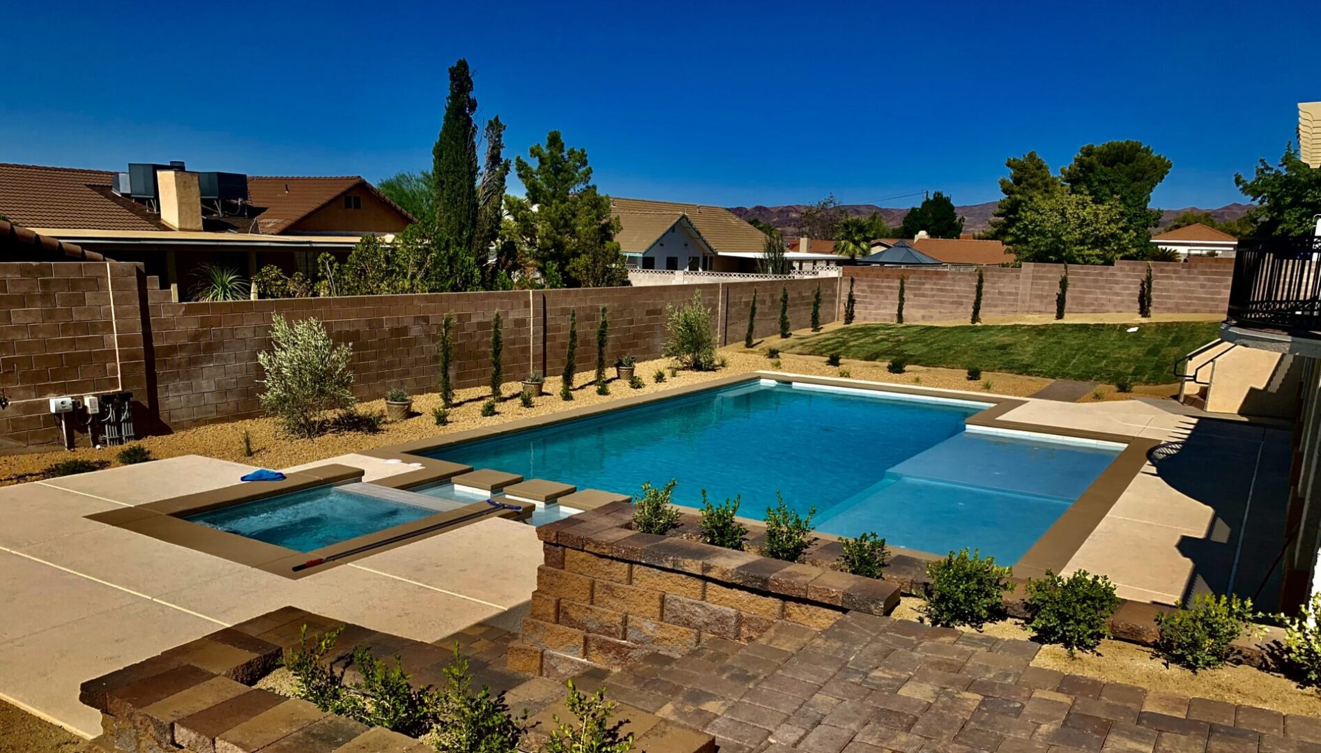 A pool with a large stone wall and a brick patio.