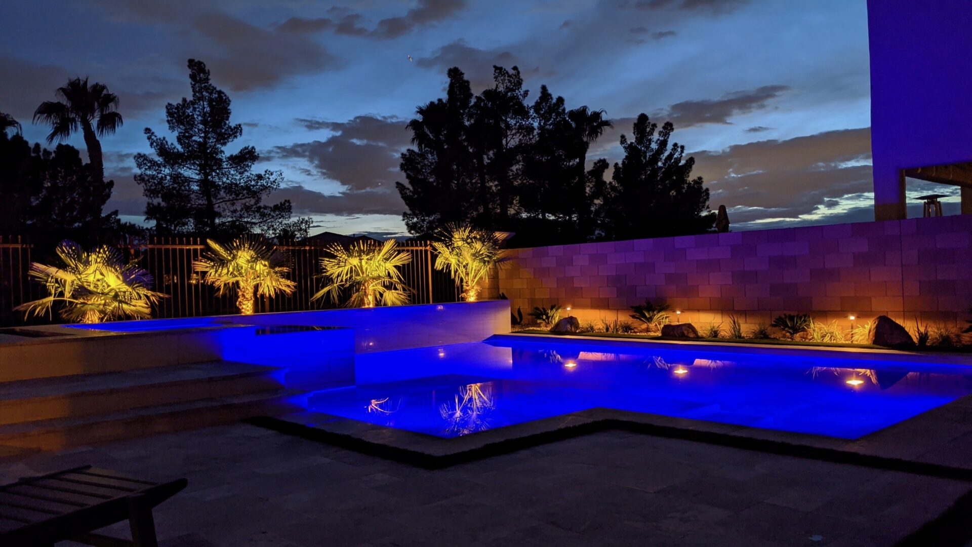 A pool with lights on and palm trees in the background.