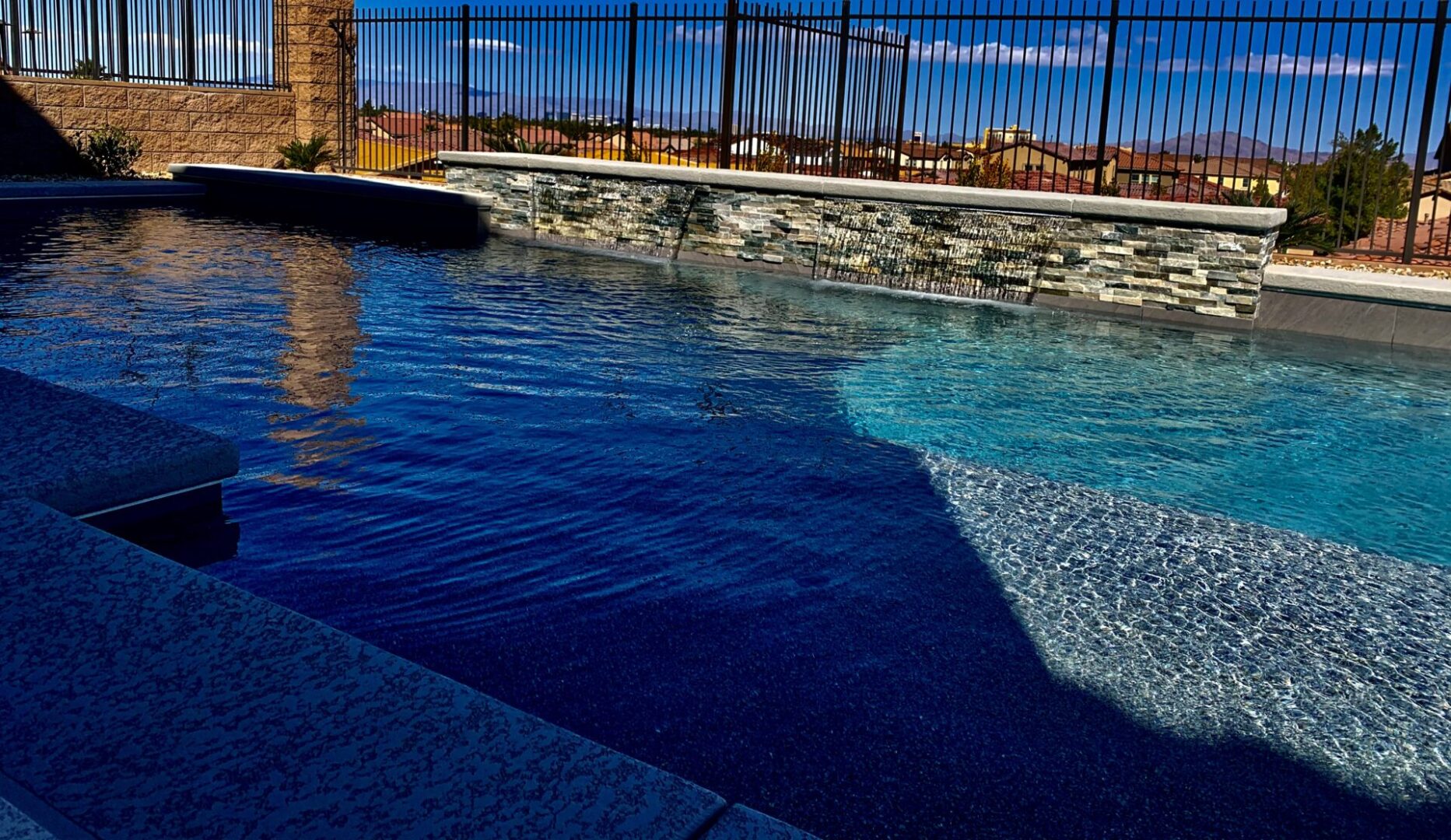 A pool with a stone wall and a fence